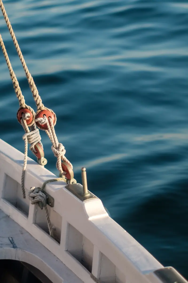 Nahaufnahme von Schiffsseilen mit roten Rollen an der Reling eines Segelbootes über dem blauen Wasser