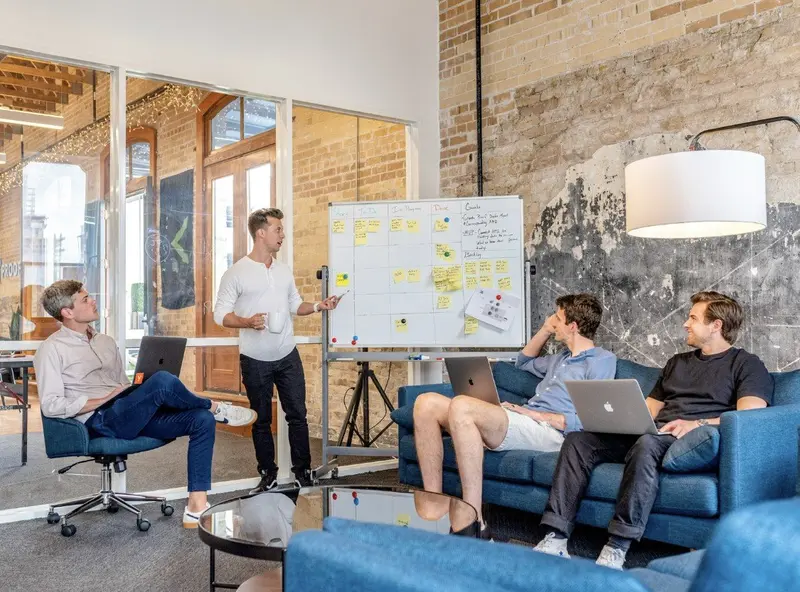 Team in moderner Loft-Büroumgebung arbeitet gemeinsam an Whiteboard mit gelben Notizzetteln