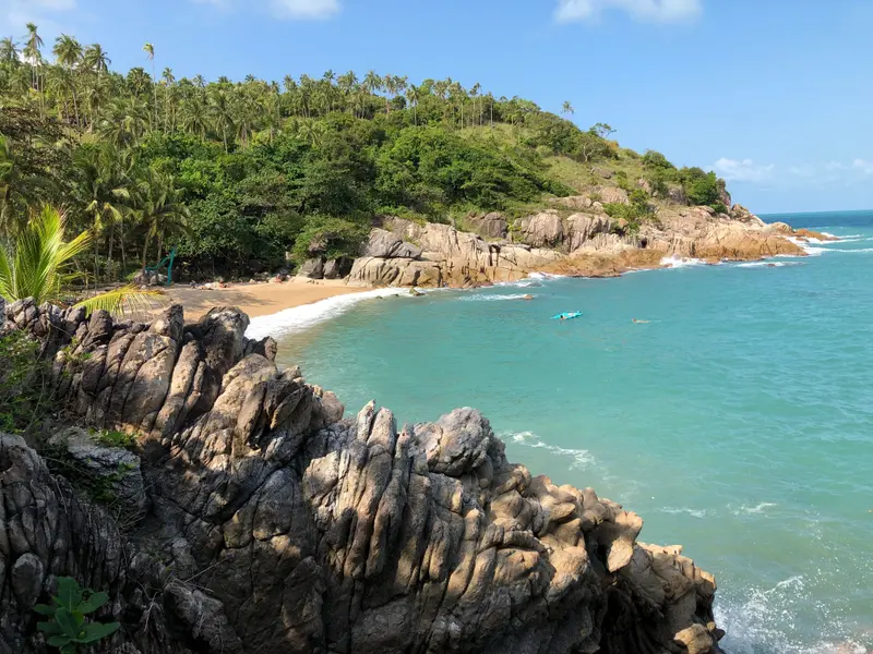 Tropische Küstenlandschaft mit türkisblauem Meer, Granitfelsen, Sandstrand und dichter Vegetation unter blauem Himmel