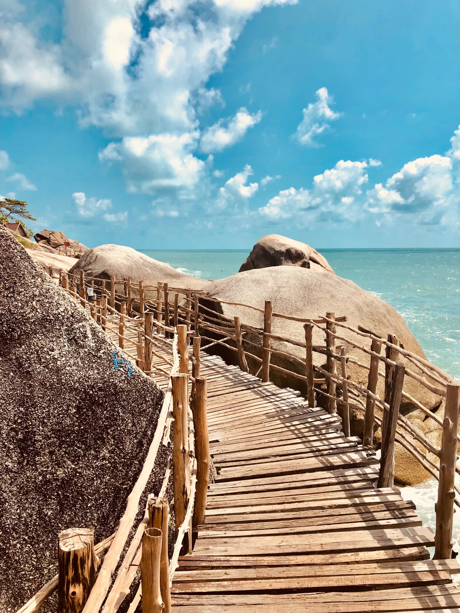 Holzsteg führt über Granitfelsen zum türkisblauen Meer, weiße Wolken am Himmel, tropisches Inselparadies