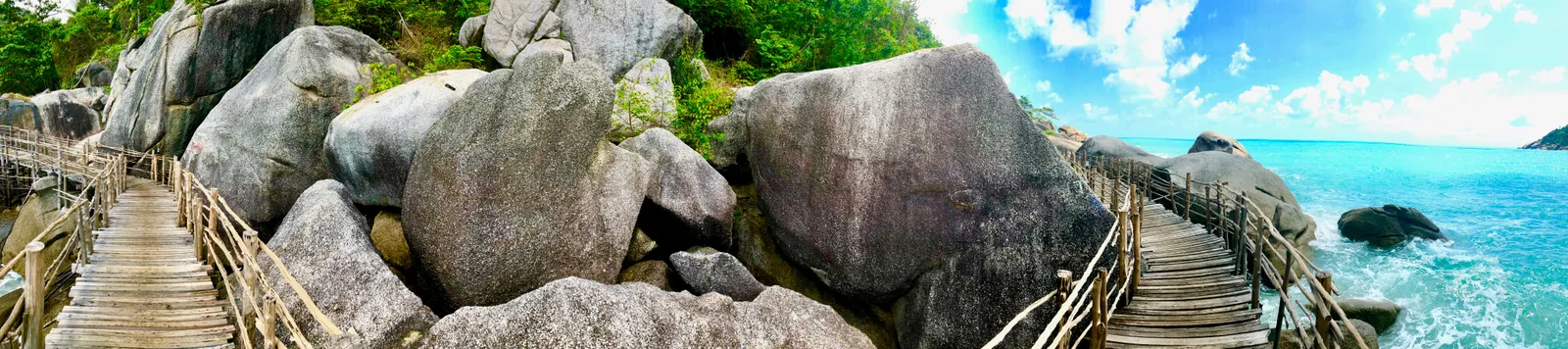 Holzsteg führt zwischen massiven Granitfelsen zu türkisblauem Meer mit idyllischer Insellandschaft
