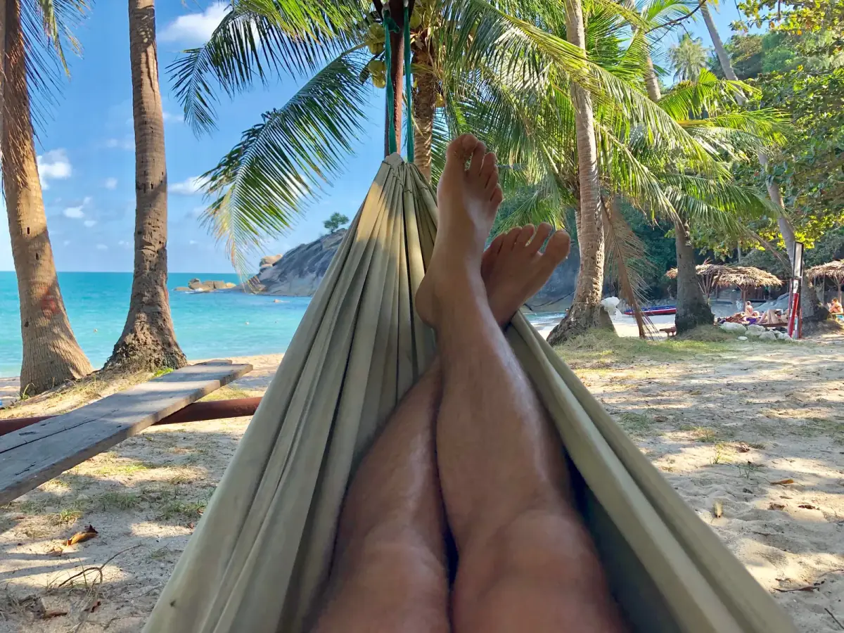 Person entspannt in Hängematte zwischen Palmen mit Blick auf türkisfarbenes Meer und Strand