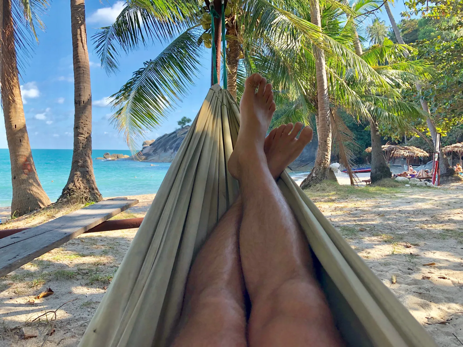 Person entspannt in Hängematte zwischen Palmen mit Blick auf türkisfarbenes Meer und Strand