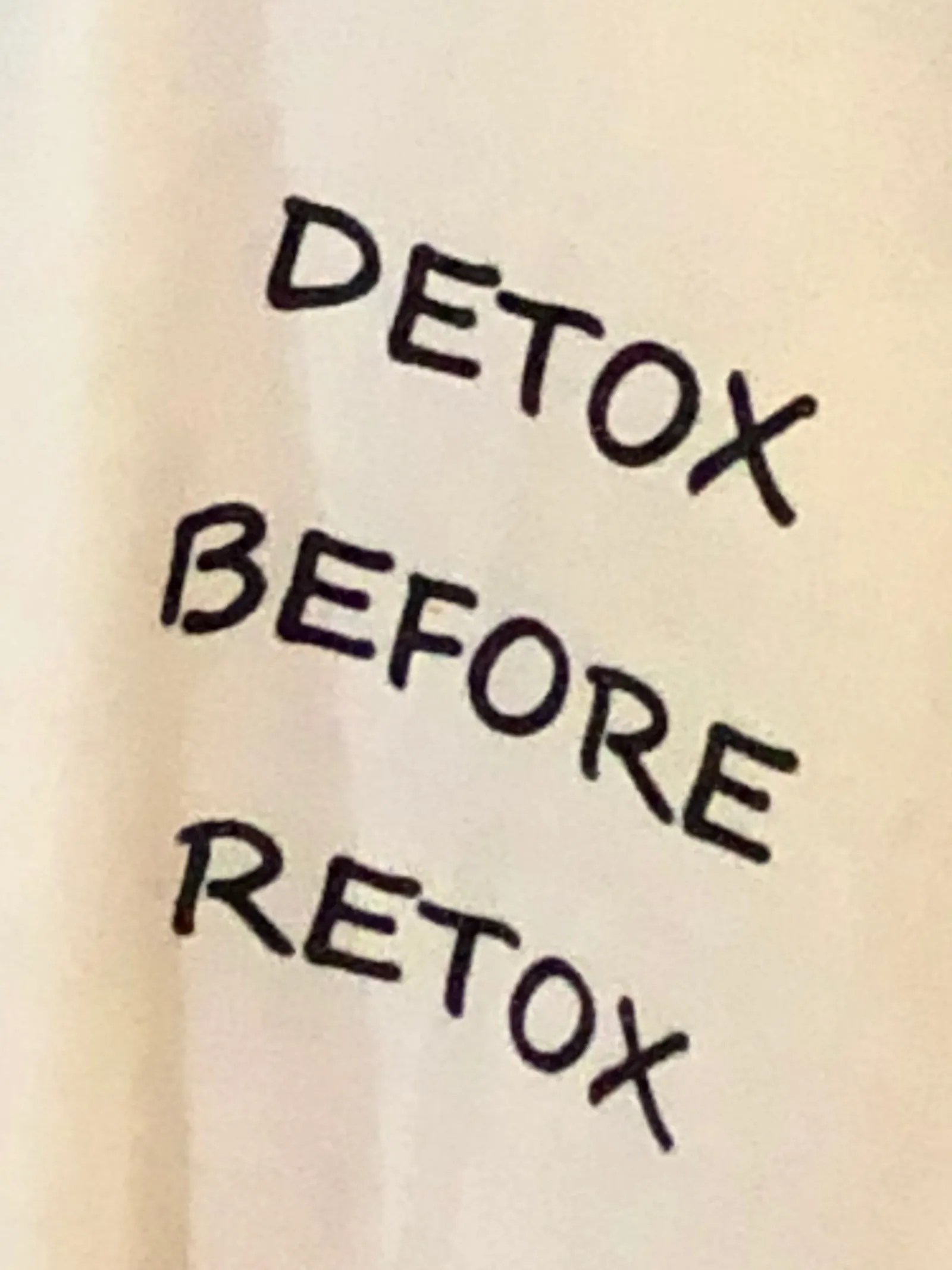 Handgeschriebener Text auf heller Oberfläche mit den Worten "DETOX BEFORE RETOX" in drei Zeilen