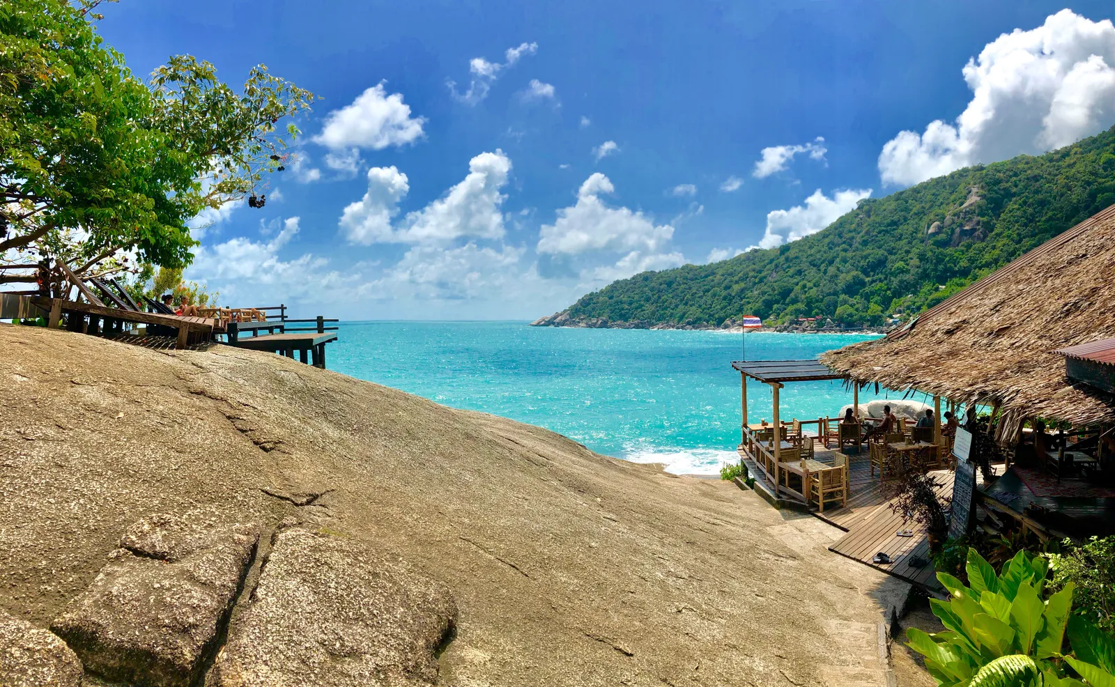 Türkisblaue Bucht mit Granitfelsen, Strohdachhütten und Holzstegen am Strand