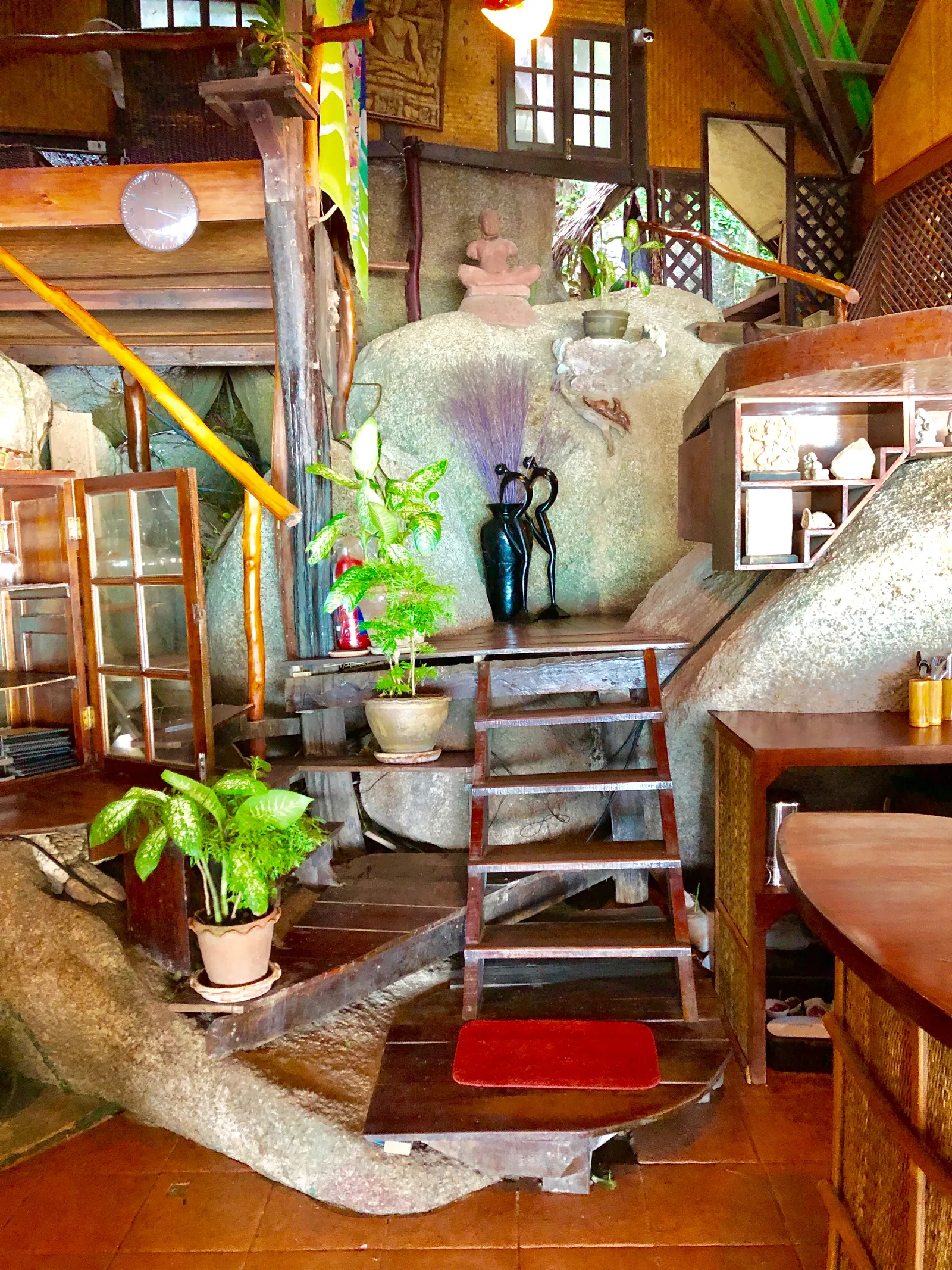 Rustikales Holzhaus mit großen Steinfiguren, Naturmaterialien und Topfpflanzen als Dekoration auf einer thailändischen Insel