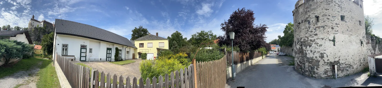 Dorfstraße mit alten Häusern, Holzzaun und mittelalterlichem Wehrturm unter blauem Himmel im Waldviertel
