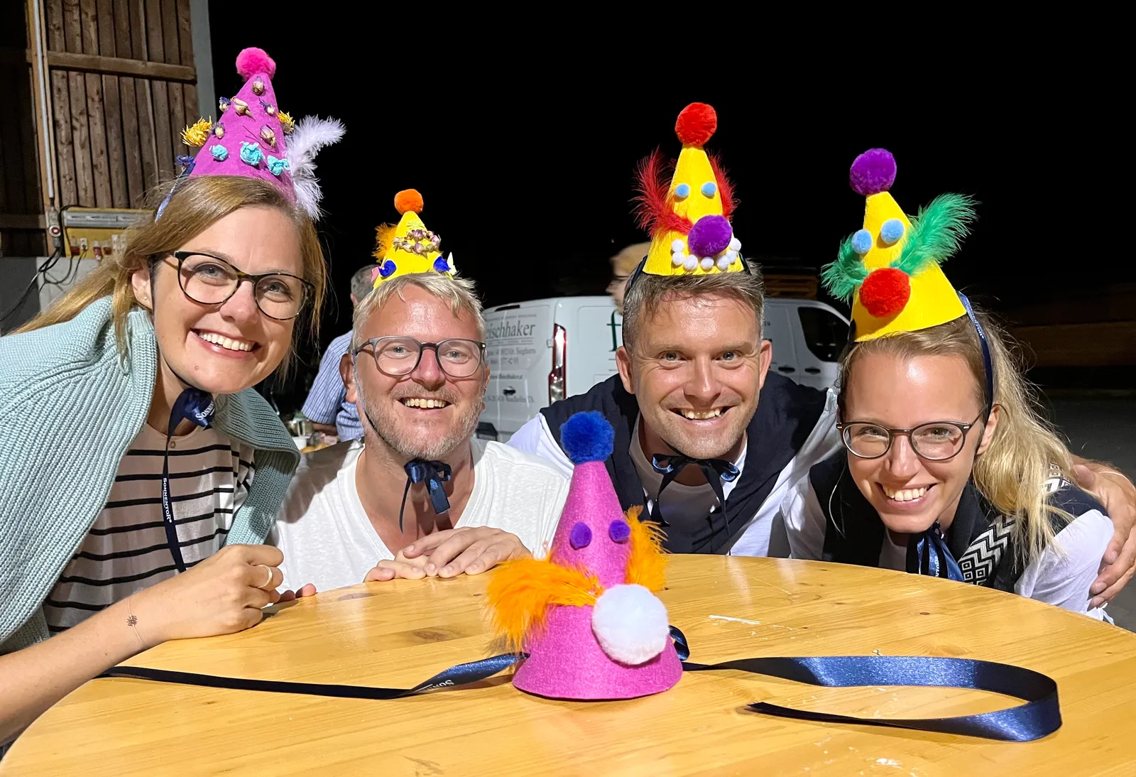 Vier Personen mit bunten selbstgebastelten Partyhüten tanzen ausgelassen an einem Tisch