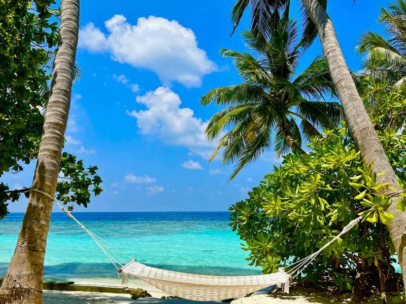 Hängematte zwischen Palmen an türkisblauem Strand mit weißen Wolken am Himmel, Sehnsucht nach Entspannung und Fernweh