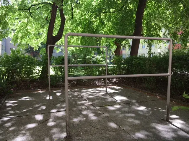 Metallgerüst aus Rohren auf gepflastertem Platz unter Bäumen mit Blattschatten in grüner Waldumgebung