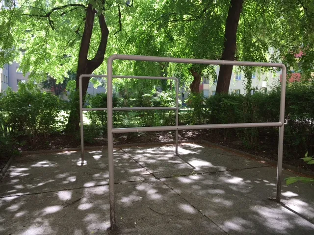 Metallgerüst aus Rohren auf gepflastertem Platz unter Bäumen mit Blattschatten in grüner Waldumgebung