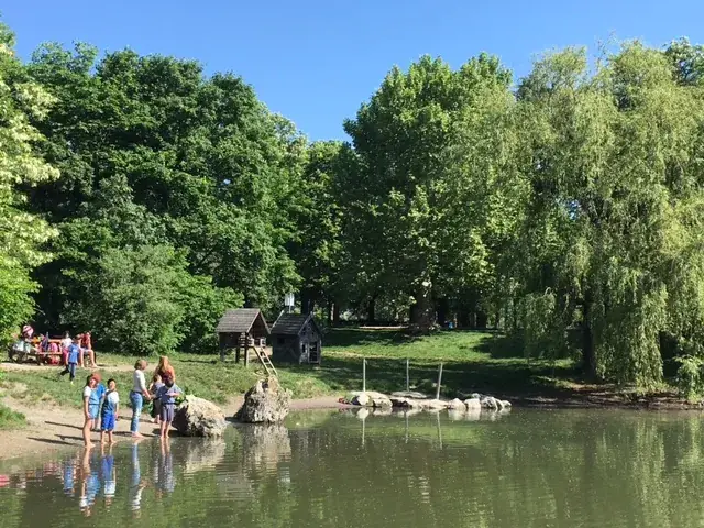 Kinder waten in einem Fluss, während andere am Ufer spielen, dahinter Wiese