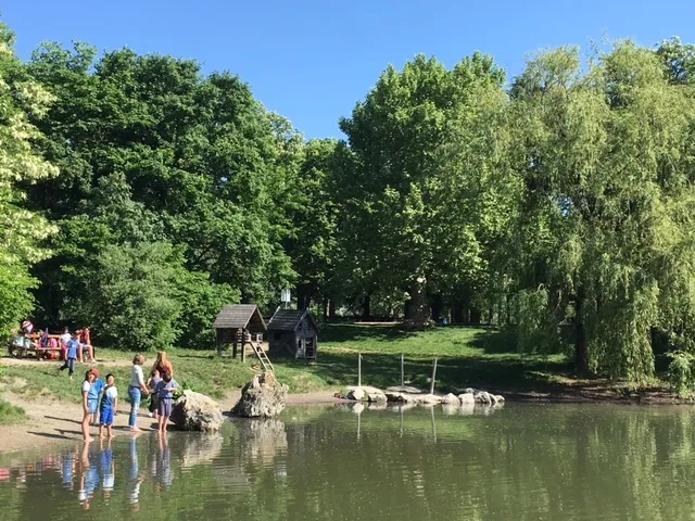 Kinder waten in einem Fluss, während andere am Ufer spielen, dahinter Wiese